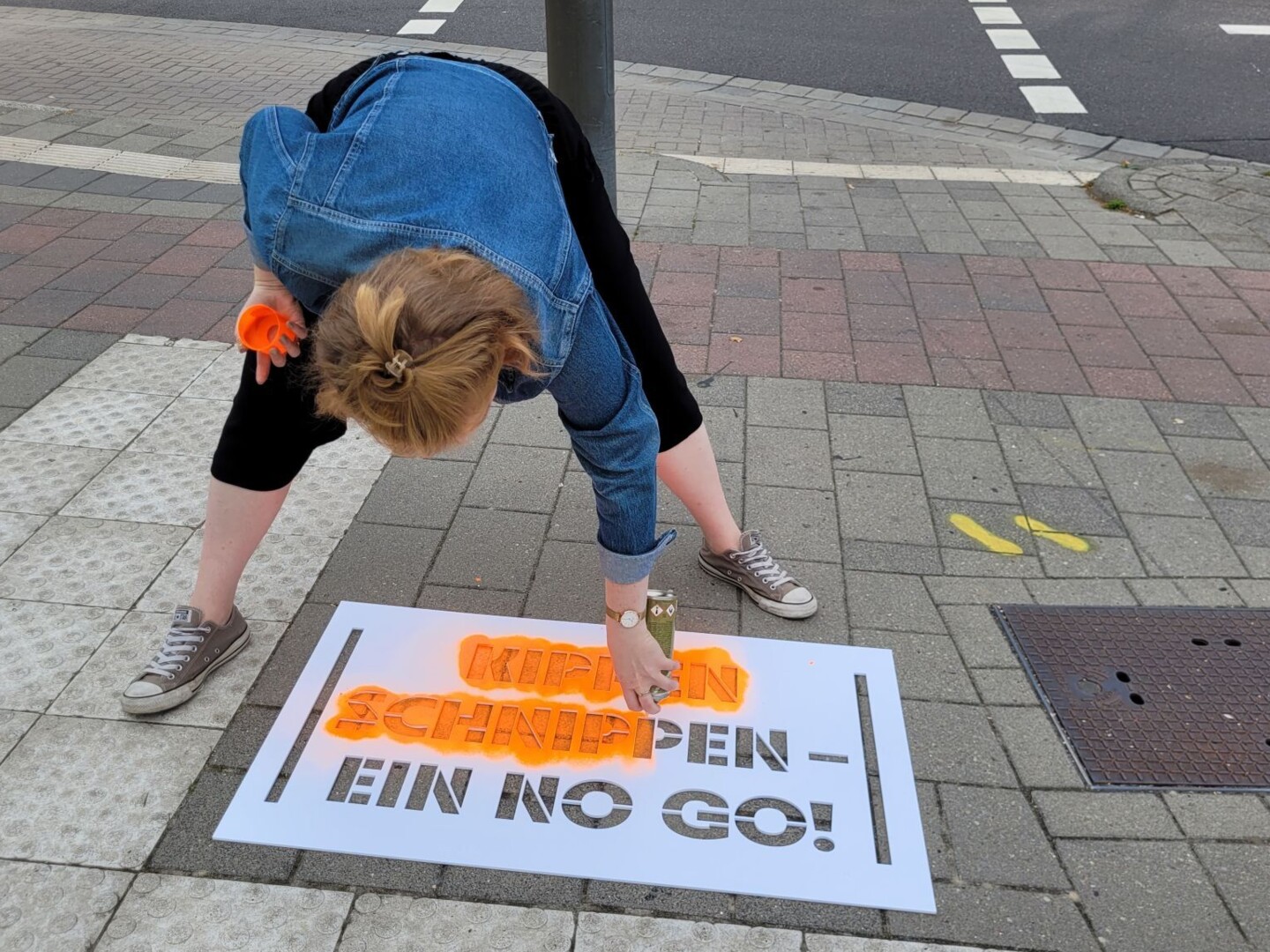 Eine Frau sprüht mit orangener Farbe den Spruch 