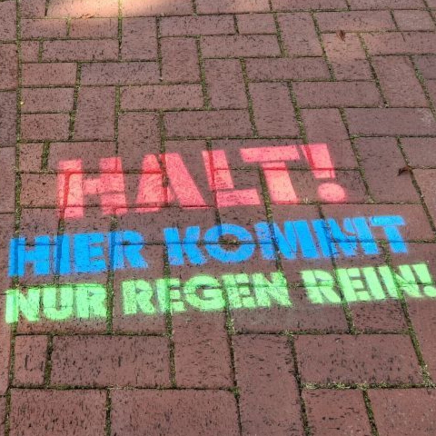 Auf einer rot gepflasterte Fl&auml;che steht in rot, blau und gr&uuml;ner Farbe der Spruch "Halt! Hier kommt nur Regen rein!"