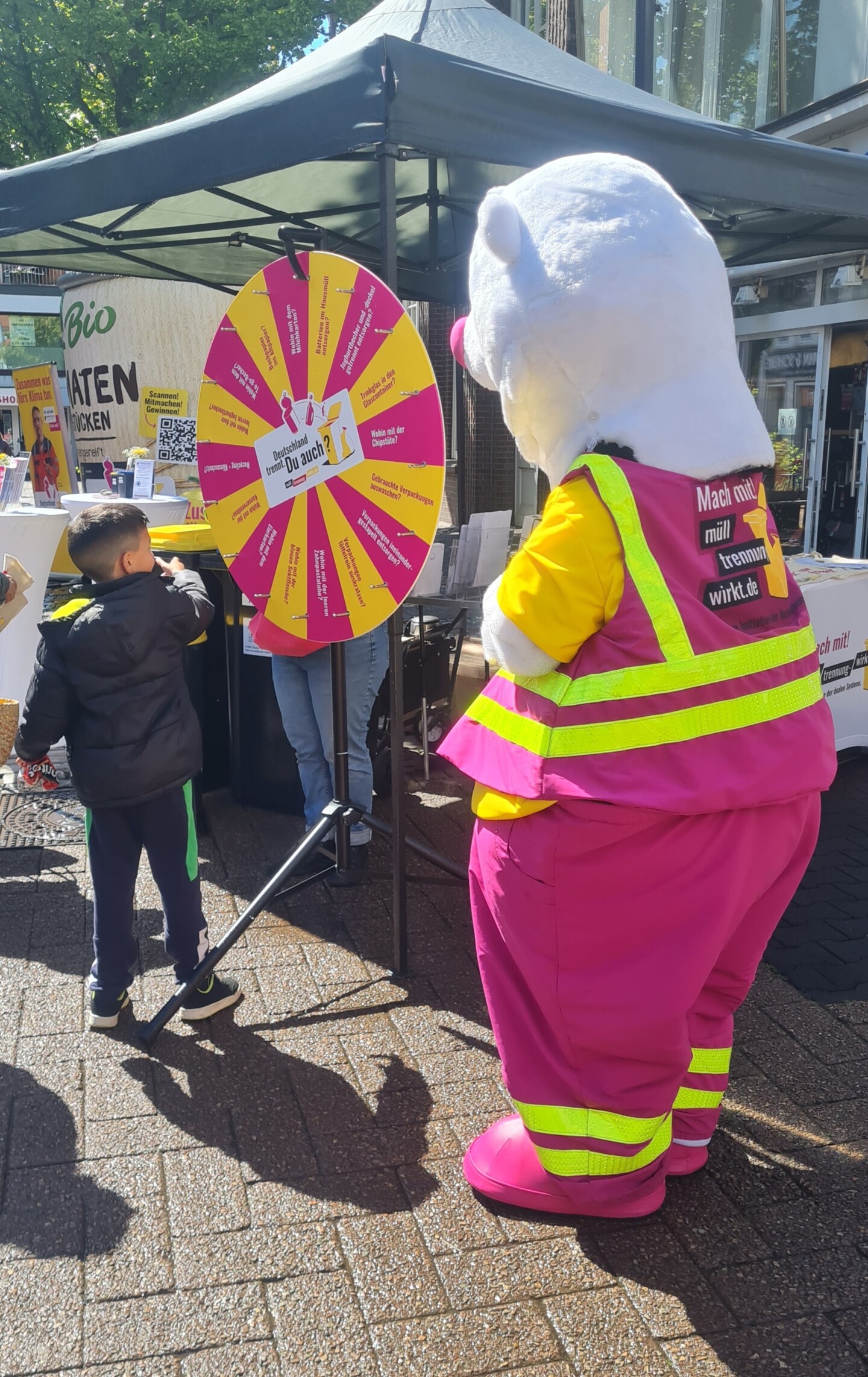 Auf einem Informationsstand dreht ein Junge an einem Glücksrad. Daneben steht eine große Figur, der sog. Trennbär.