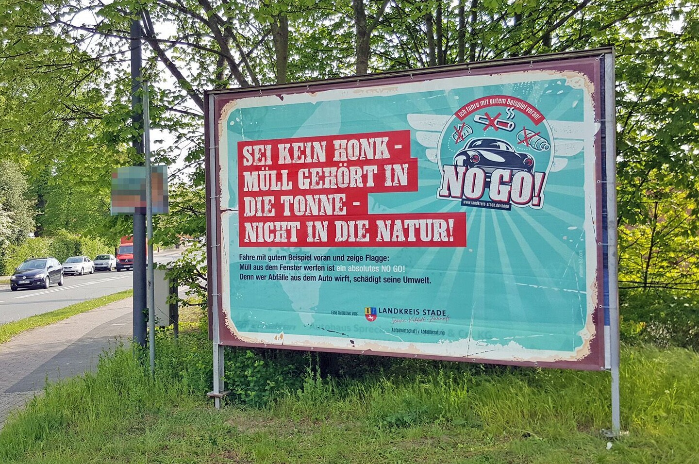 Ein Großplakat zur NO Go Kampagne, das im Grünbereich neben einer Straße aufgestellt ist.