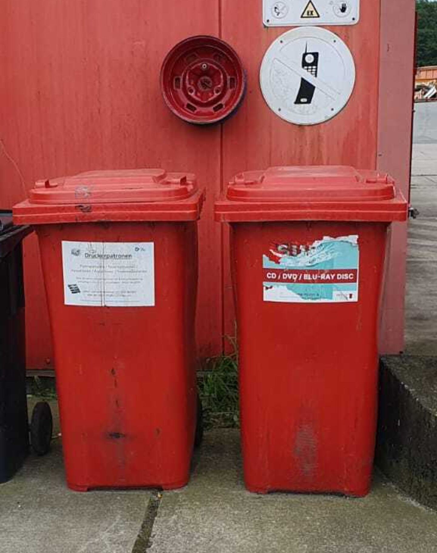 Zwei rote Tonnen für CDs und DVDs nebeneinander vor einem roten Container.