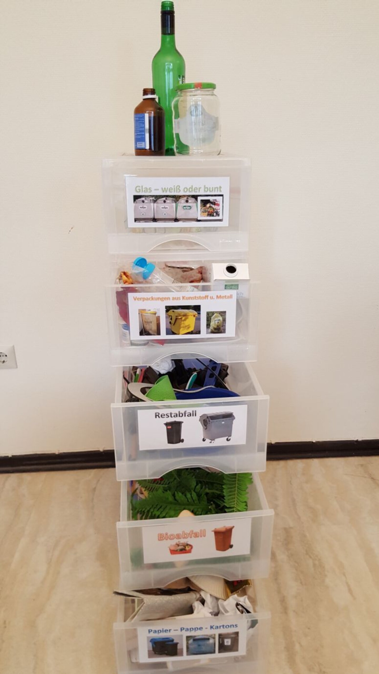 Eine Plastikbox mit mehreren Schubladen, in denen verschiedene Abfälle je nach Abfallart sind. Auf der Schublade ist jeweils eine Markierung aufgeklebt, welche Abfälle darin sind.
