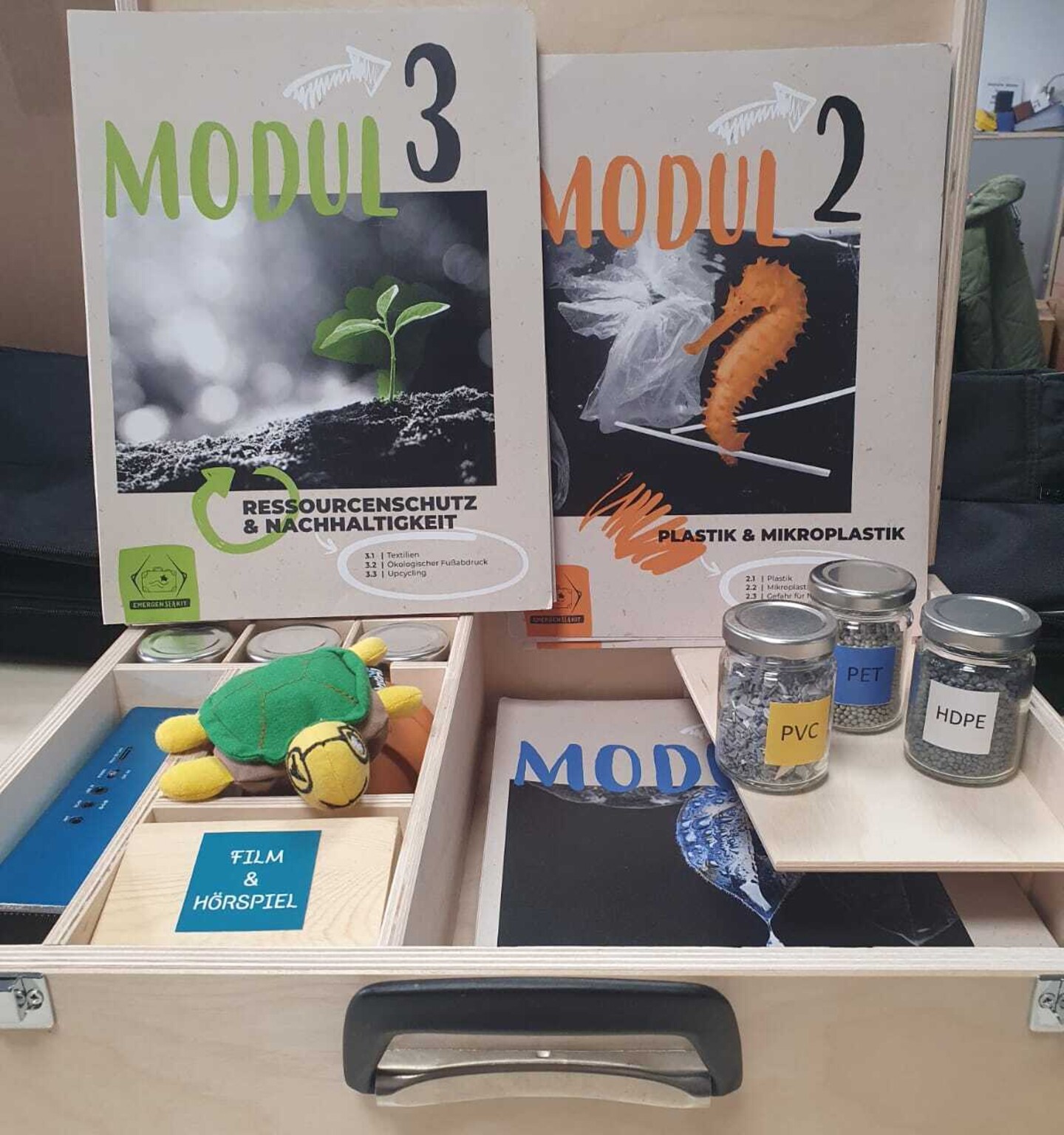 Der geöffnete EmergenSea-Kit Koffer. Schraubgläser mit verschiedenen Kunststoffgranulaten, eine Stoffschildkröte, Papiermappen zu den Themen
