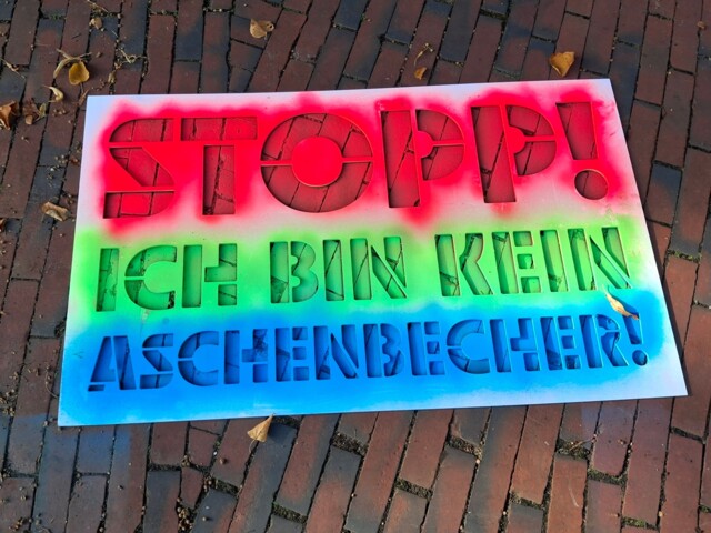 Eine Schablone mit dem Spruch Stopp! (in roter Farbe), Ich bin kein (in grüner Farbe), Aschenbecher (in blauer Farbe).