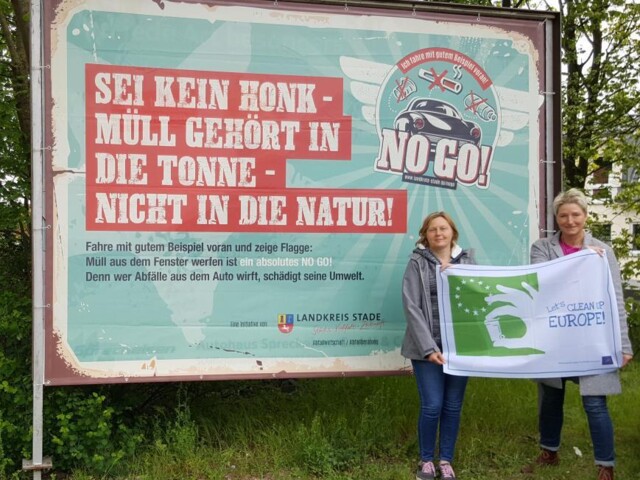 Vor dem Großplakat zur Kampagne stehen zwei Frauen mit der Flagge zur Lets Clean up Europe in den Händen.&nbsp;