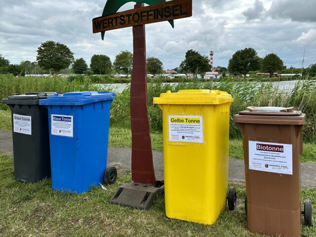 verschiedene Abfalltonnen neben Holzplalme