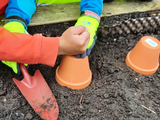 Ein Hochbeet, Kinderhände, Tonblumentopf auf der Erde eines Hochbeetes