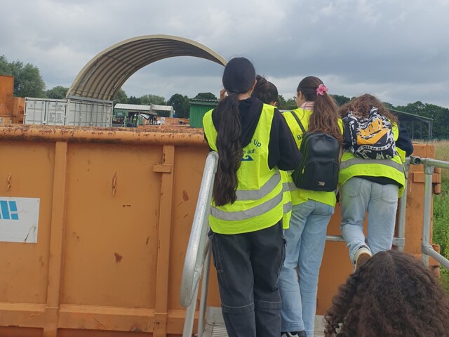 Jugendliche schauen in eine orangefarbenen Container.